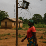 A rural African woman walks past a disconnected solar panel installation beside her home, highlighting the disconnect between climate finance pledges and on-ground energy access.