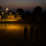African village at dusk, half illuminated by solar lamps and half in darkness, children walking toward light, symbolising just energy transition.